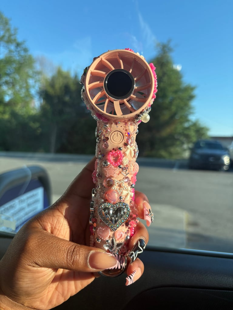 Hand holding an ornate pink and gold decorative hand pipe with floral and jeweled embellishments outdoors