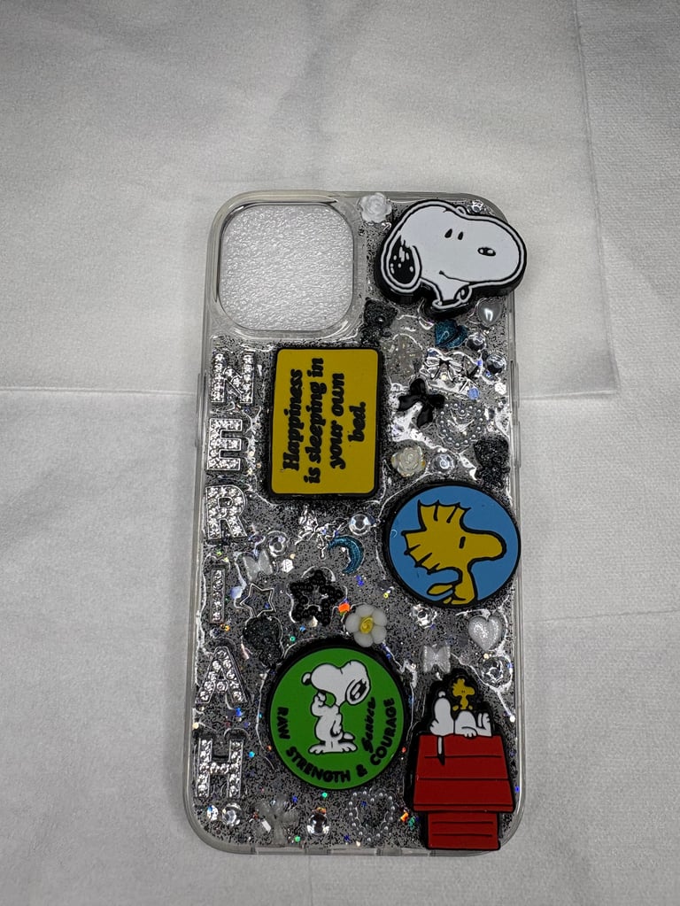 Peanuts-themed phone case with Snoopy, Woodstock, and character patches on a silver glitter background